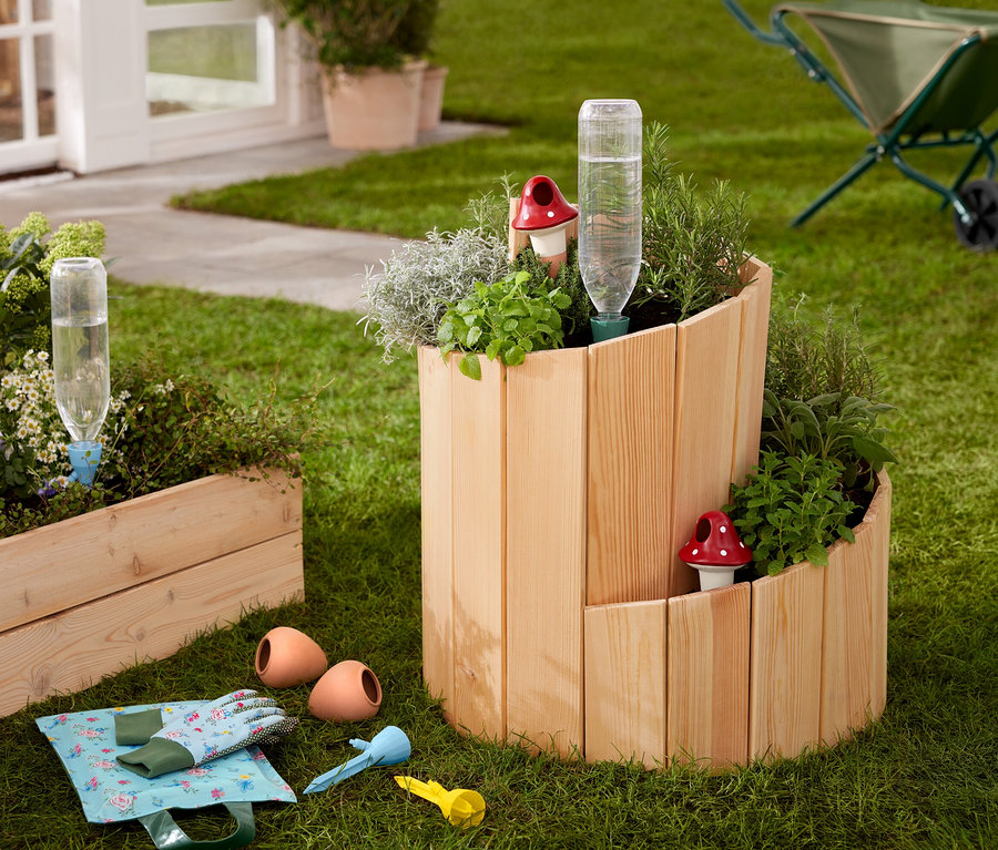 Egy füvön egy fából készült magas ágyás »Csiga«, gyógynövényekkel és zöldségekkel beültetve.