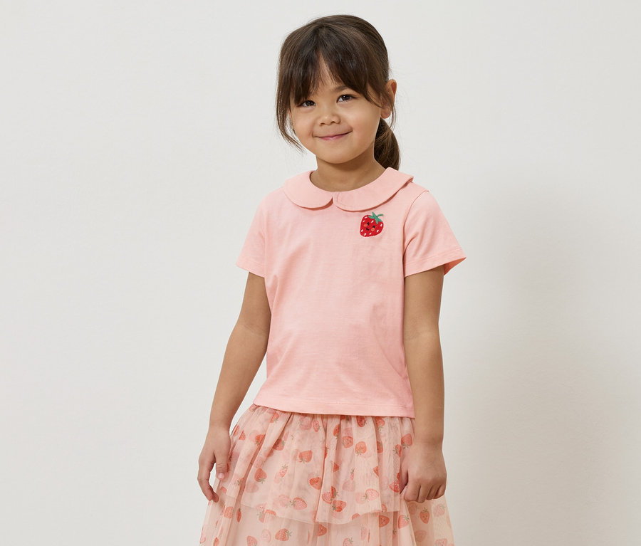 Kislány rózsaszín pólóban, eperrátéttel és rózsaszín, epres mintás szoknyában.