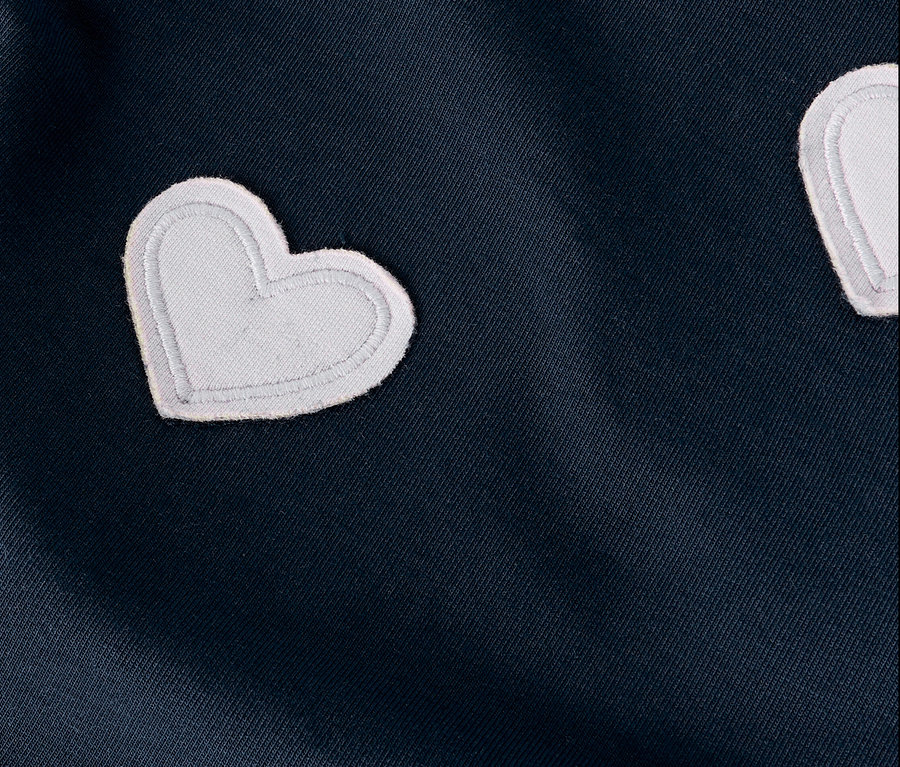 Sötétkék anyag közeli képe fehér szív alakú applikációkkal.