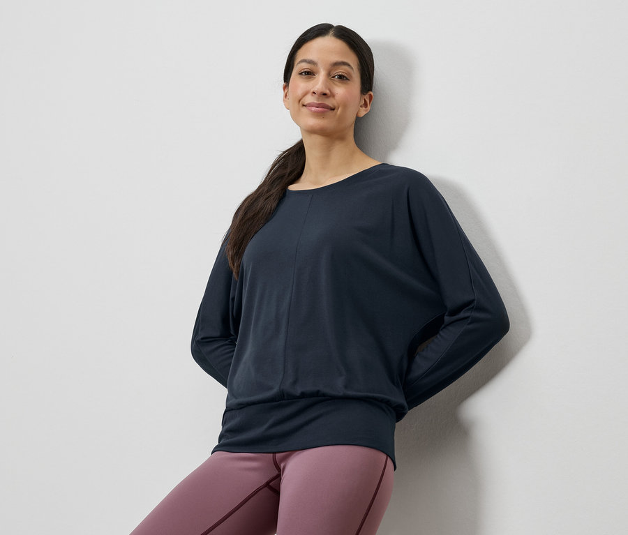 Nő sötétkék hosszú ujjú felsőt és rózsaszín leggingset visel.