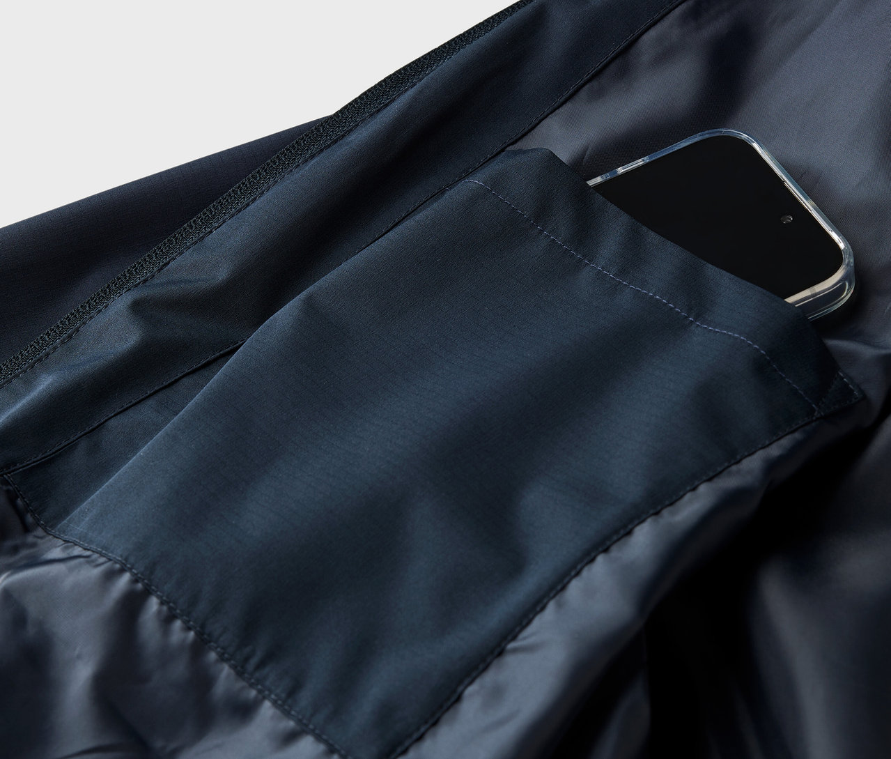 Közeli kép egy sötétkék kabátról, zsebben okostelefonnal.