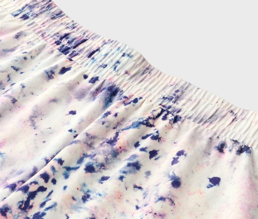 Rövidnadrág közelképe elasztikus derékpánttal és lila, kék és rózsaszín batikolt mintával.