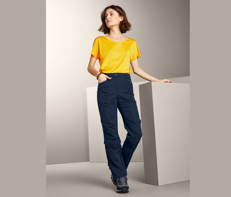 Nő sötétkék, 2 az 1-ben funkcionális nadrágban és sárga pólóban pózol.