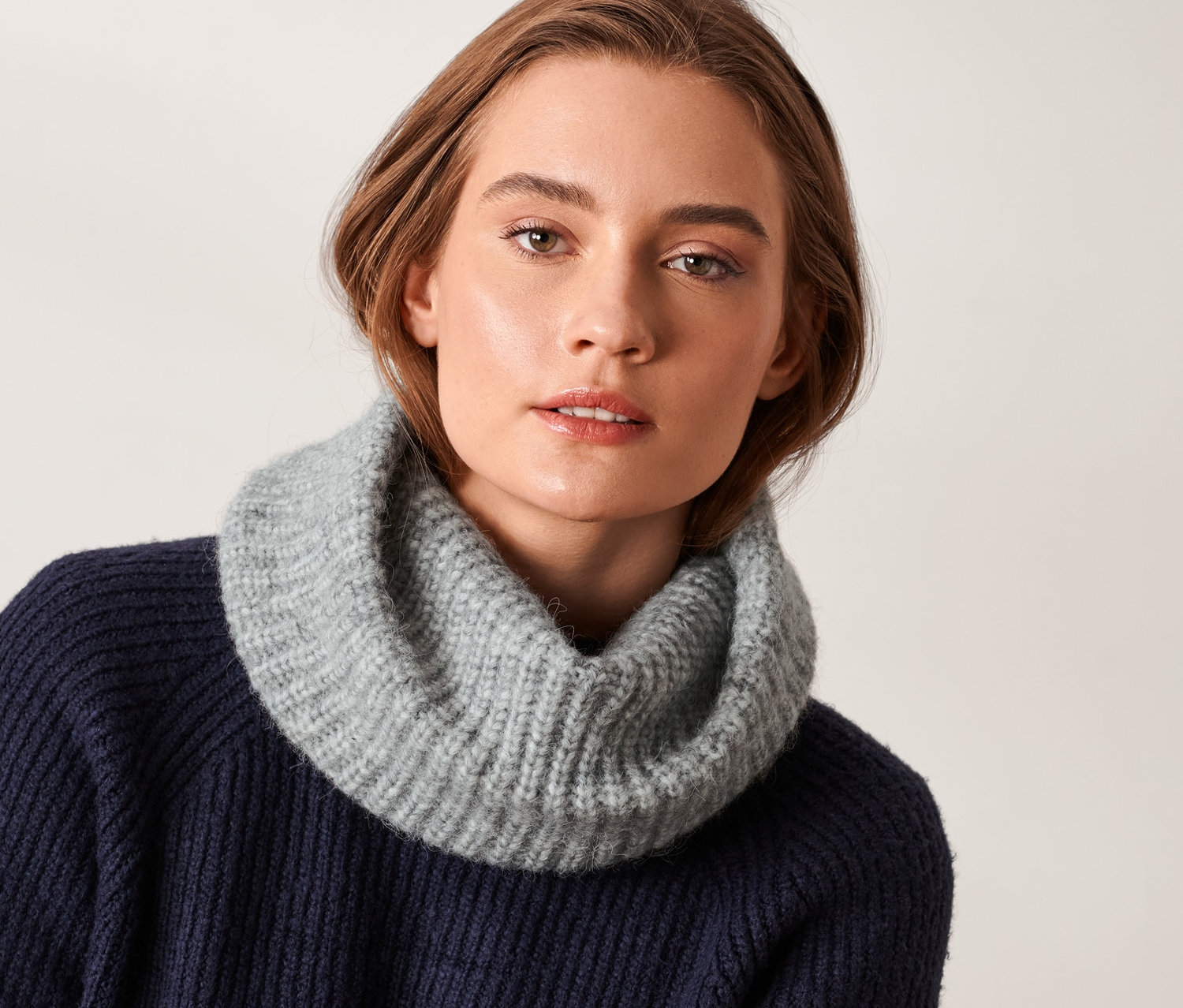 Nő visel egy szürke kötött csősálat.