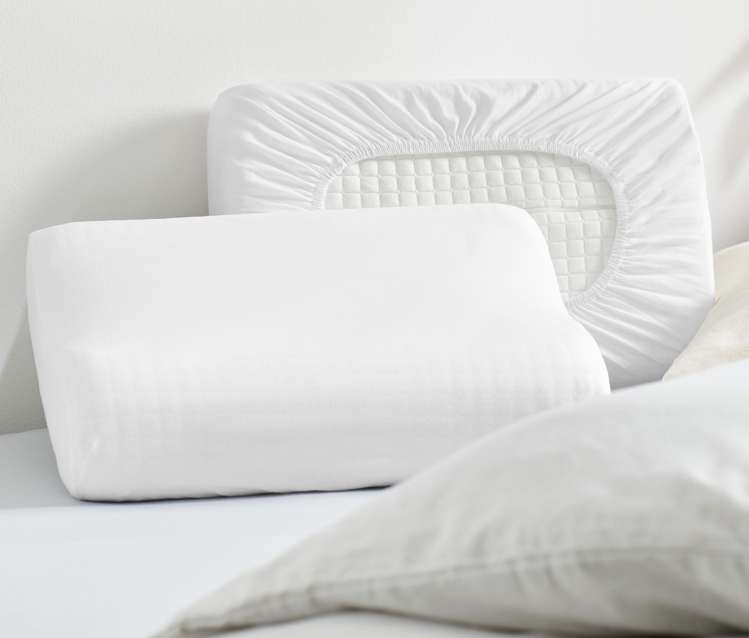 Két fehér gumis jersey párnahuzat fekszik egy ágyon.