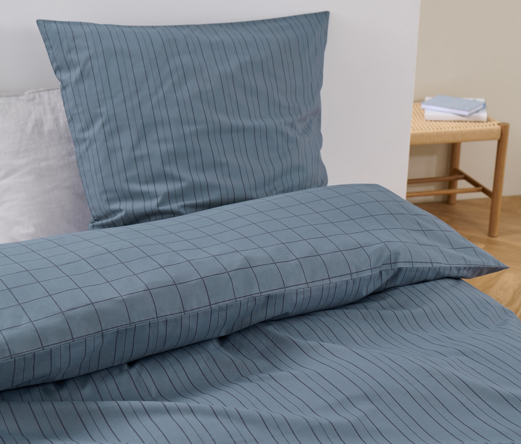 Kék, csíkos és kockás mintázatú, normál méretű renforcé ágynemű egy ágyon.