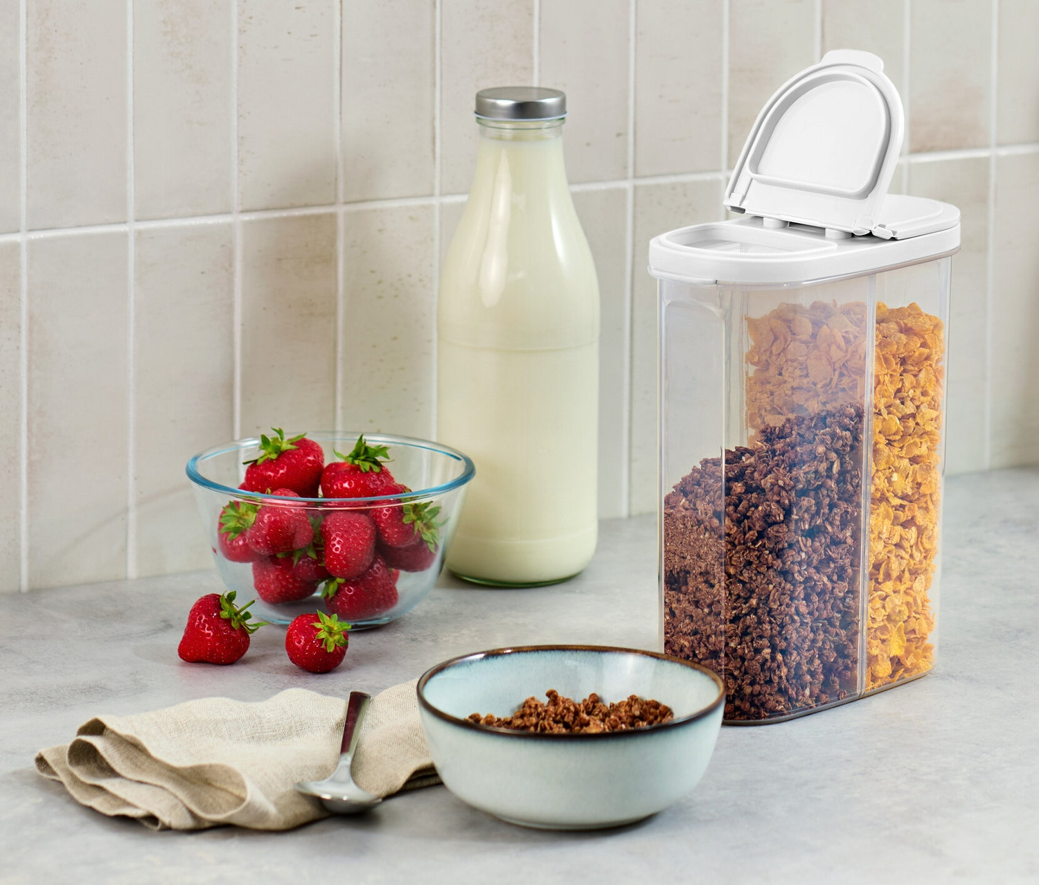 A konyhapulton egy 2 az 1-ben tárolódoboz, egy tál eper, egy üveg tej és egy tál müzli található.