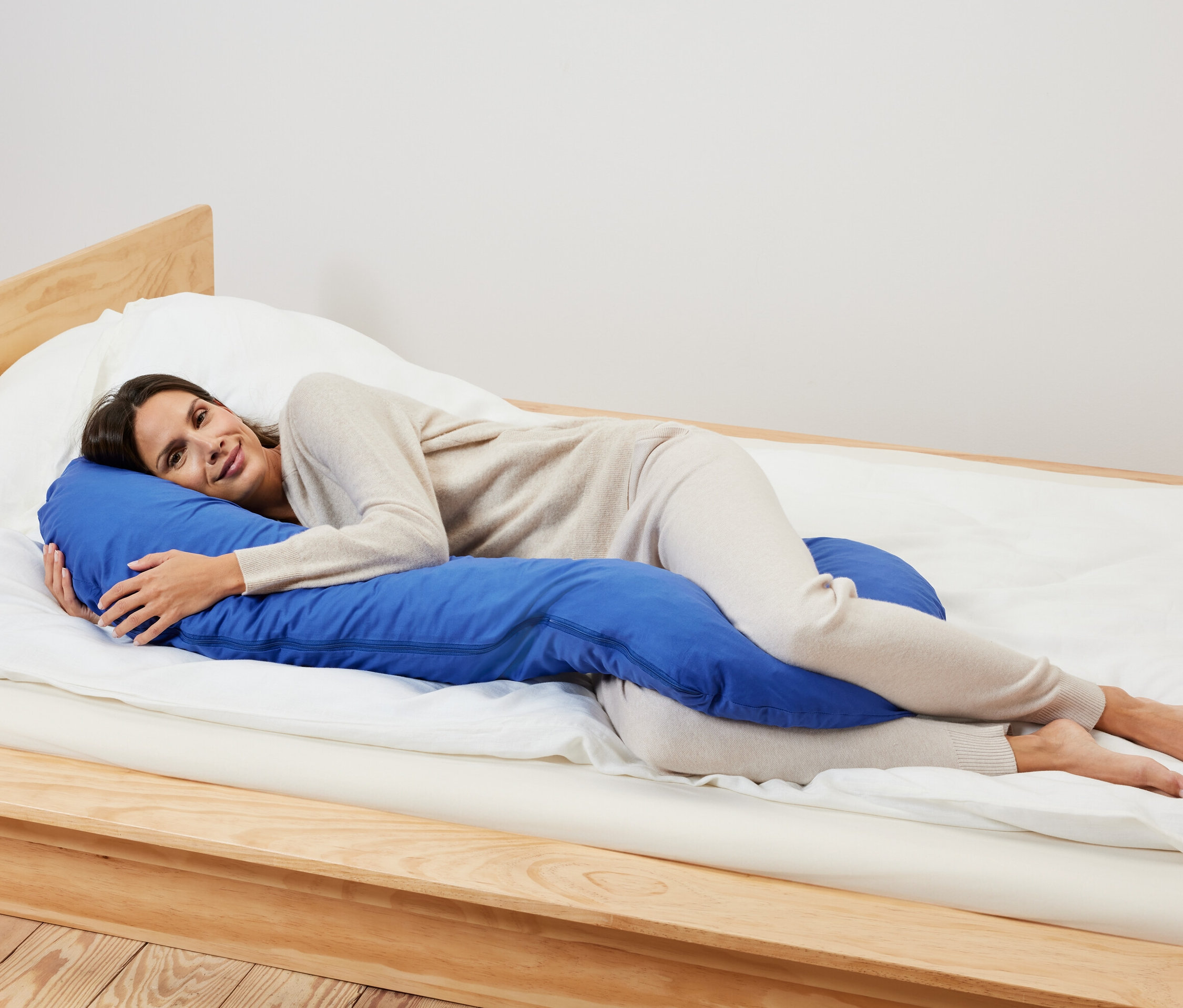 Nő fekszik az ágyon az oldalán, és egy kék XL párnát ölel oldalt alvóknak.