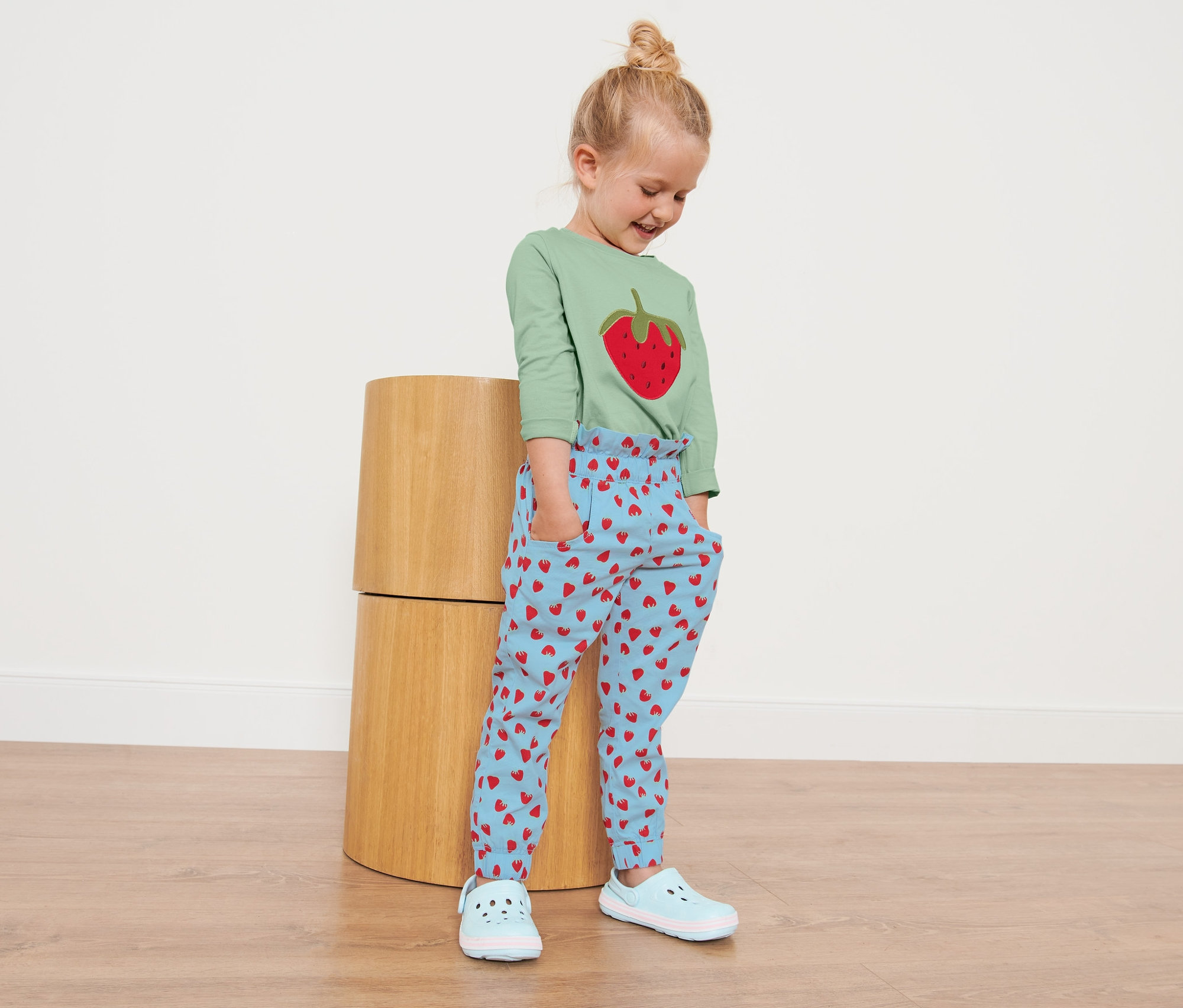 Egy kislány áll, és kisgyerek paperbag nadrágot visel, epermintával.