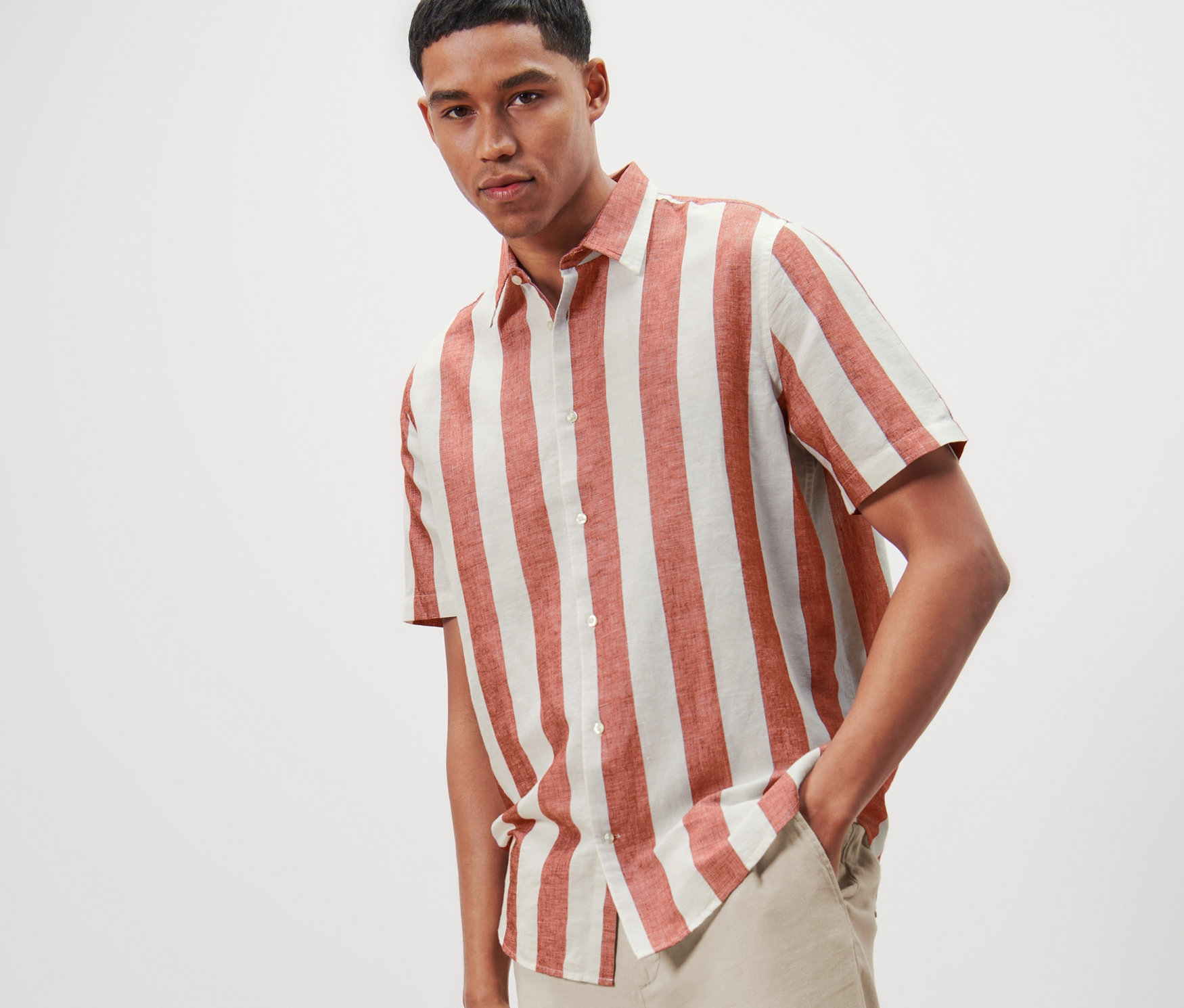 Férfi pózol csíkos, rövid ujjú, lenvászon tartalmú ingben és világos nadrágban.