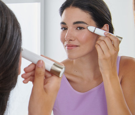 Egy nő elektromos szemöldökformázóval igazítja a szemöldökét a tükör előtt.