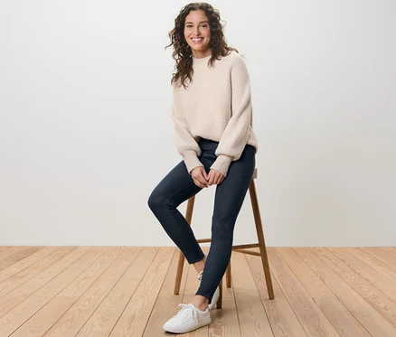 Nő ül egy széken, farmerhatású bélelt leggingset és pulóvert visel.