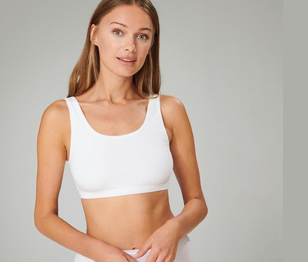 Hosszú barna hajú nő visel egy fehér SCHIESSER bustier melltartót és fehér alsóneműt, előre néz.