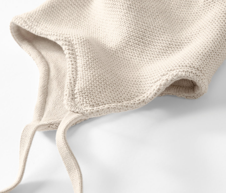 Egy krémszínű kötött sapka és sál részletének közeli képe fehér háttéren.