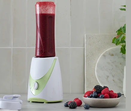 Smoothie készítő piros smoothie-val és egy tál bogyóval.