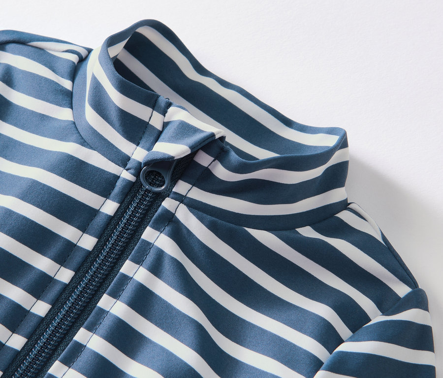 Kék-fehér csíkos, 80-as UV-védelemmel ellátott gyermek kezeslábas részlete cipzárral.