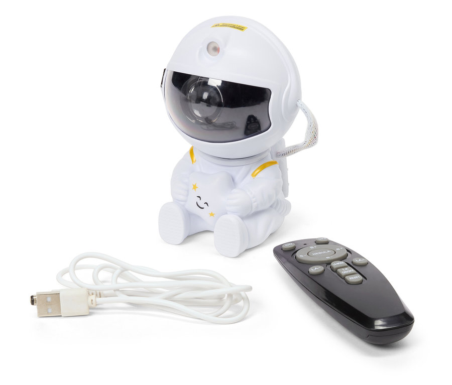 Egy fehér éjszakai égbolt projektor űrhajós formában ül egy fekete távirányító és egy fehér USB-kábel mellett.