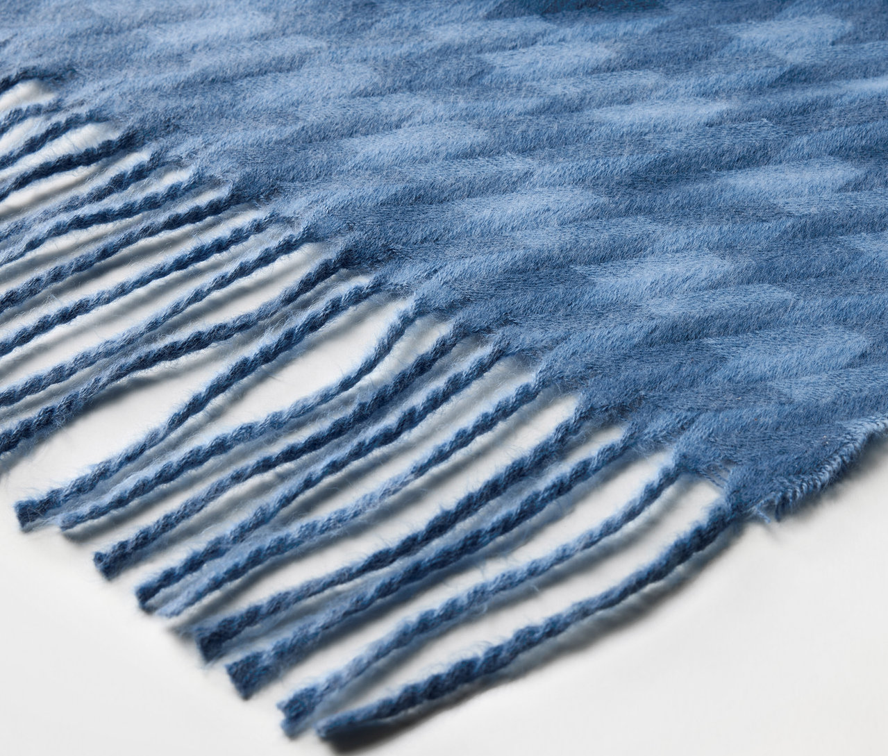 Kék, rojtokkal ellátott sál részlete.