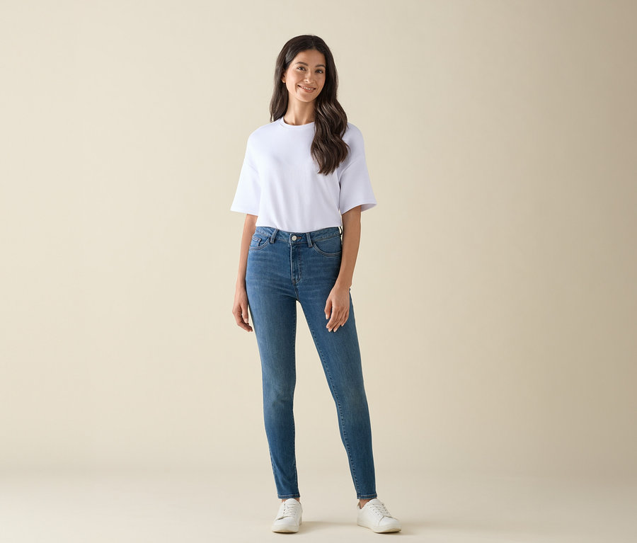 Egy nő pózol fehér pólóban, kék farmerben és fehér tornacipőben.