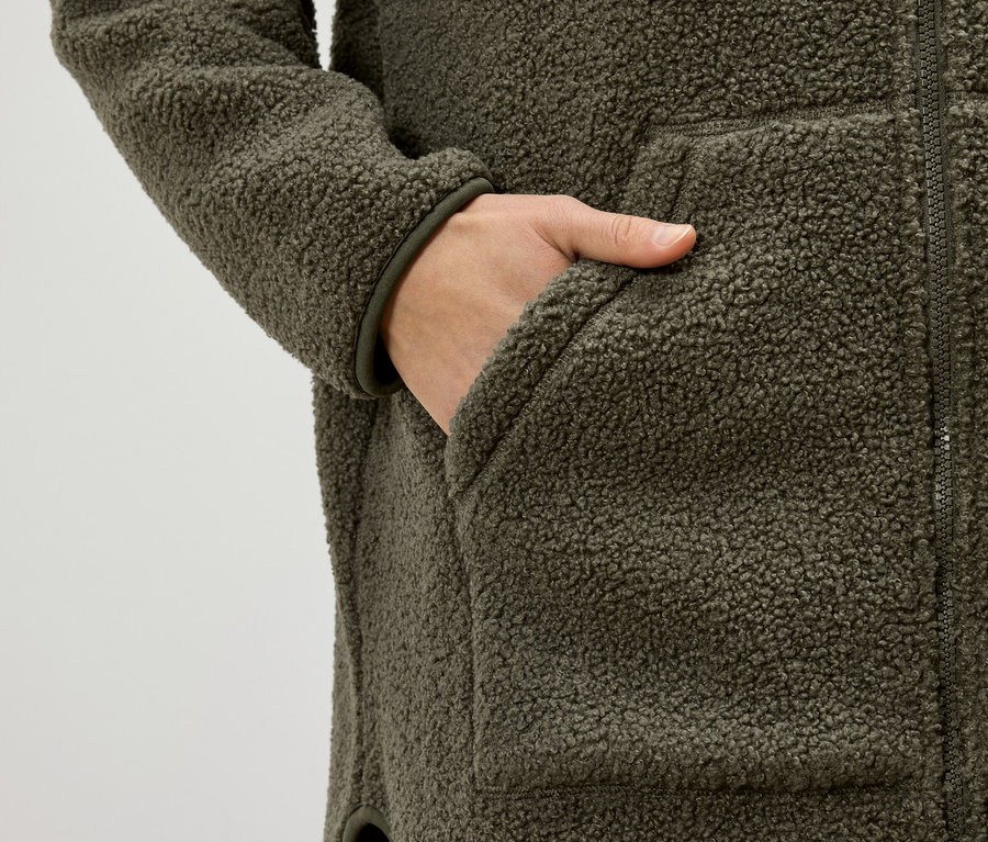 Kéz egy olívazöld, báránybőr hatású kabát zsebében.
