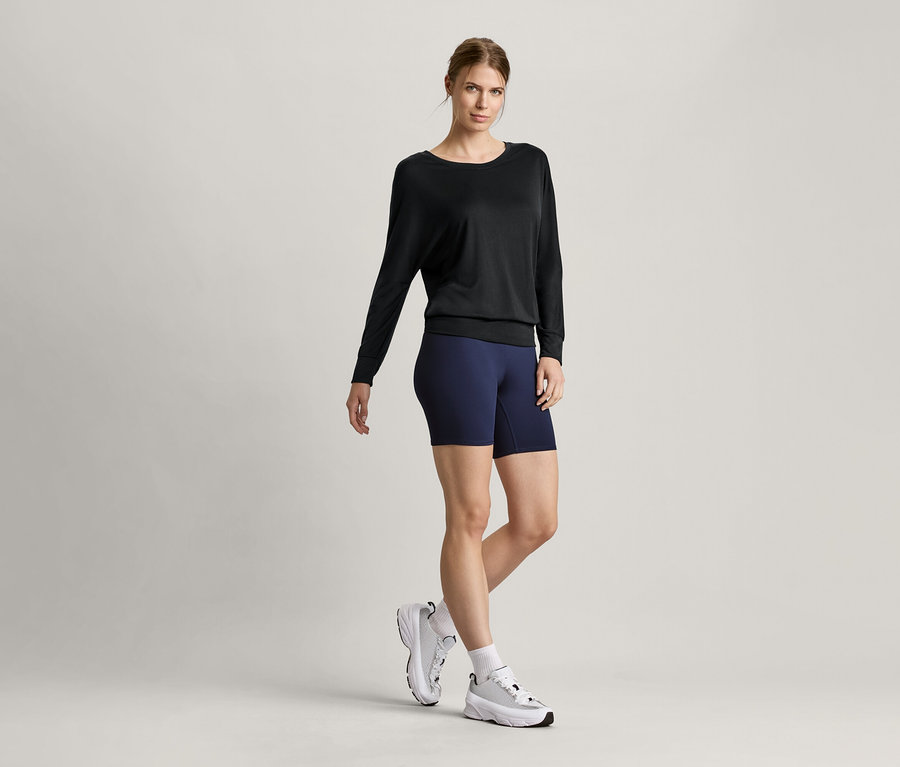 Nő visel fekete női denevér ujjú sportfelsőt és rövid sportnadrágot.