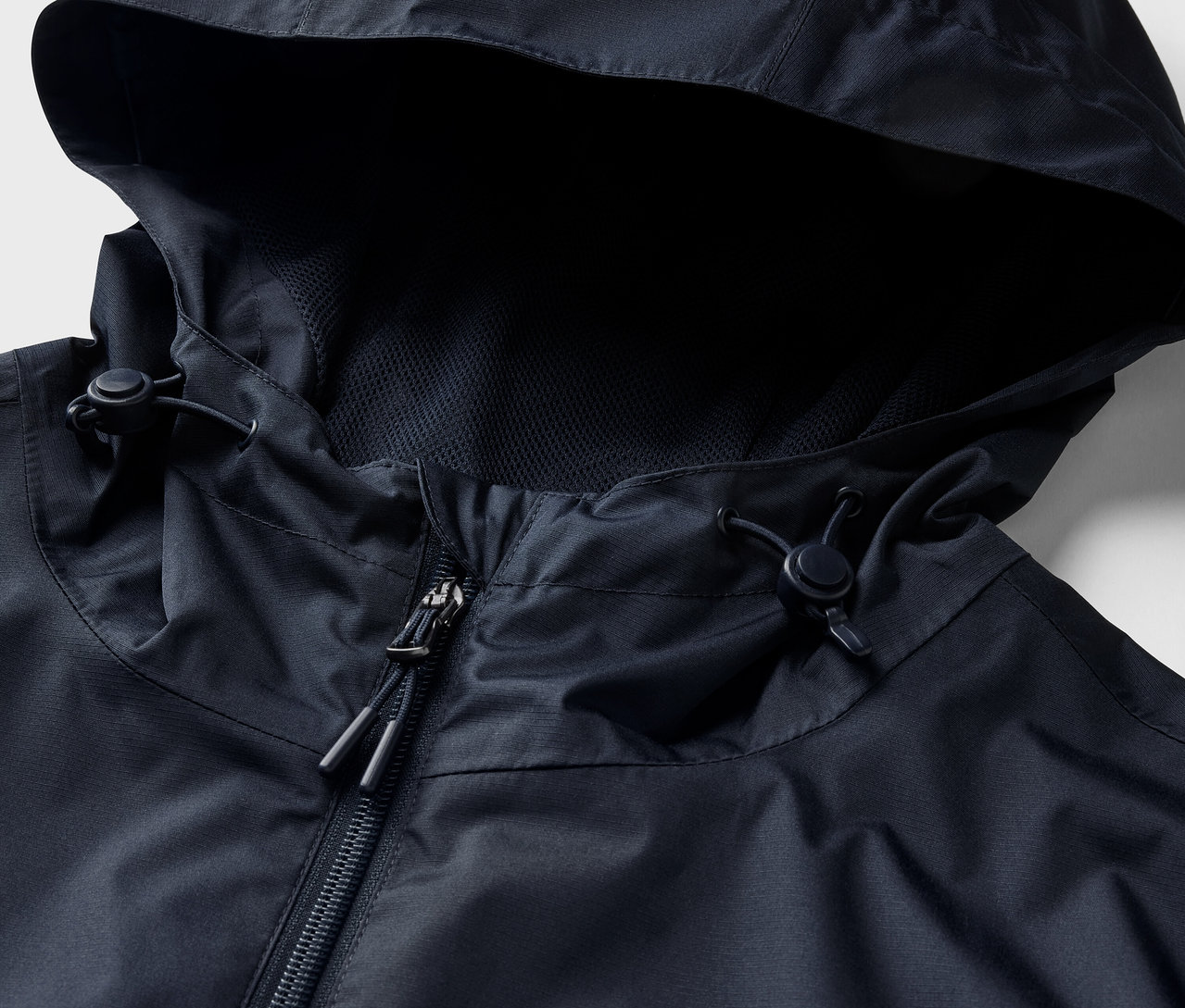 Egy tengerészkék esőkabát részlete, kapucnival és cipzárral.