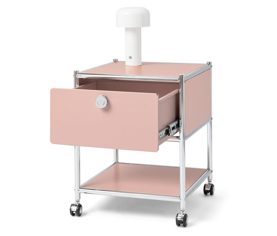 Rózsaszín éjjeliszekrény nyitott fiókkal és egy fehér lámpával a tetején.