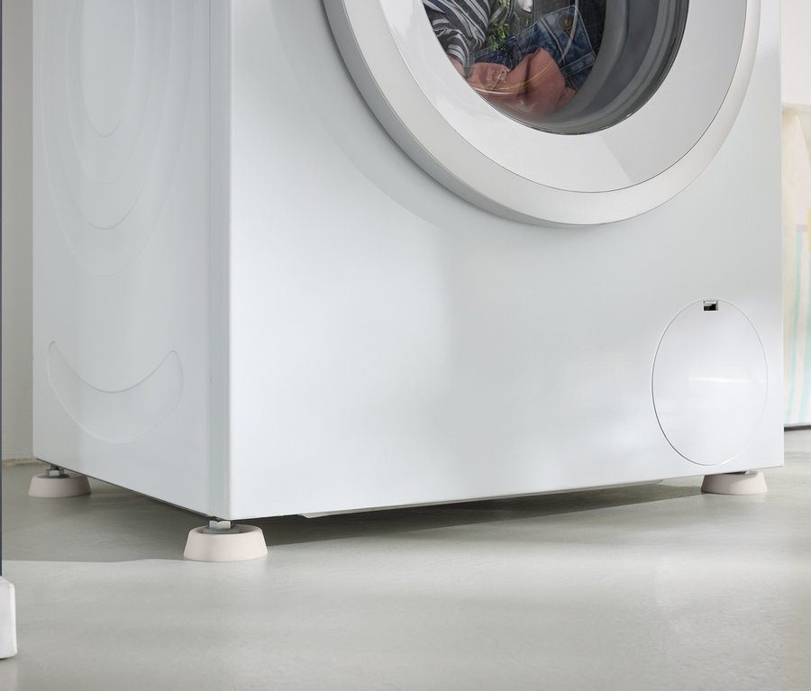 Egy fehér mosógép részlete, amely fehér alátéteken áll egy szürke padlón.