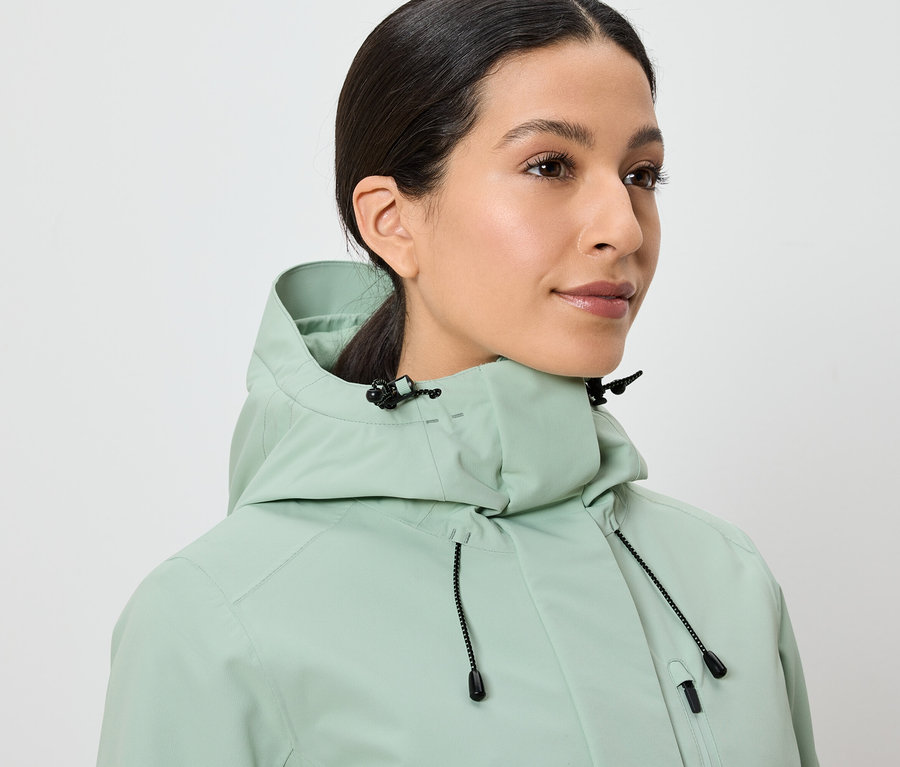 Egy nő világoszöld, kapucnis kabátot visel.