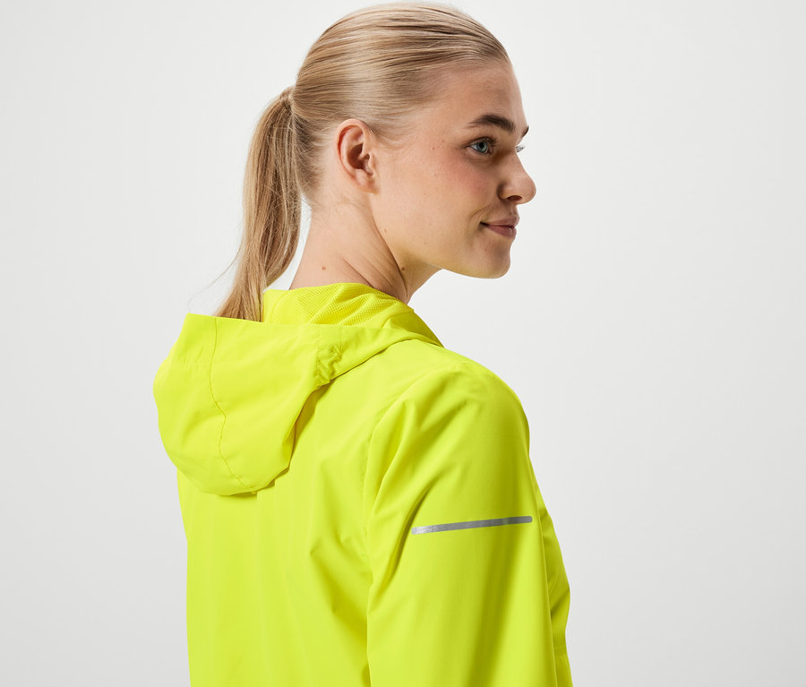 Szőke hajú, lófarokba kötött nő neonsárga kapucnis kabátot visel.