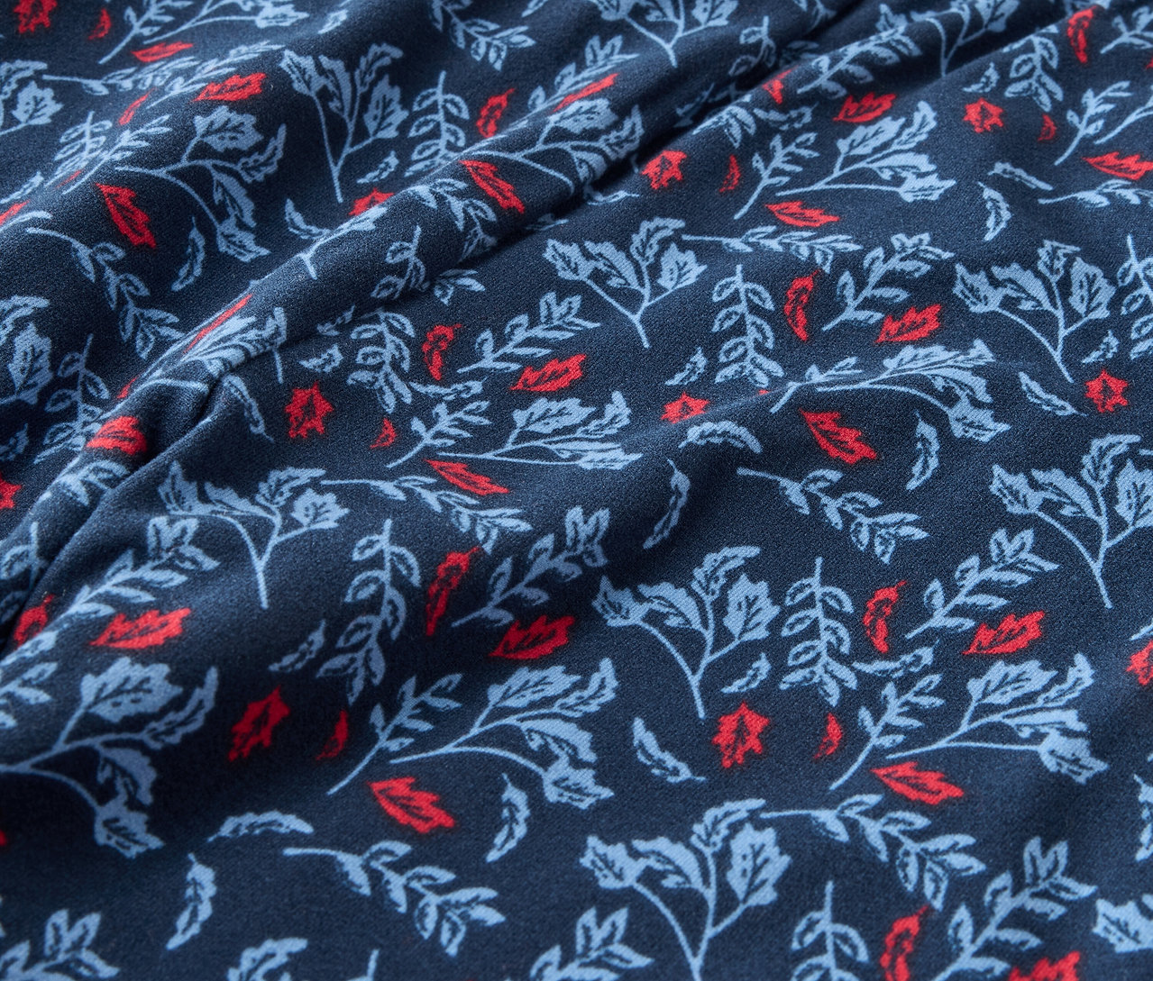 Egy sötétkék szövet közeli képe piros és világoskék levelekkel nyomtatva.