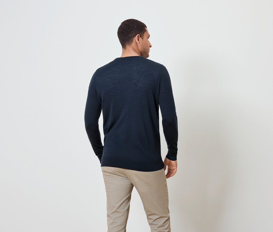 Egy férfi hátulról, sötétkék pulóvert és bézs nadrágot visel.