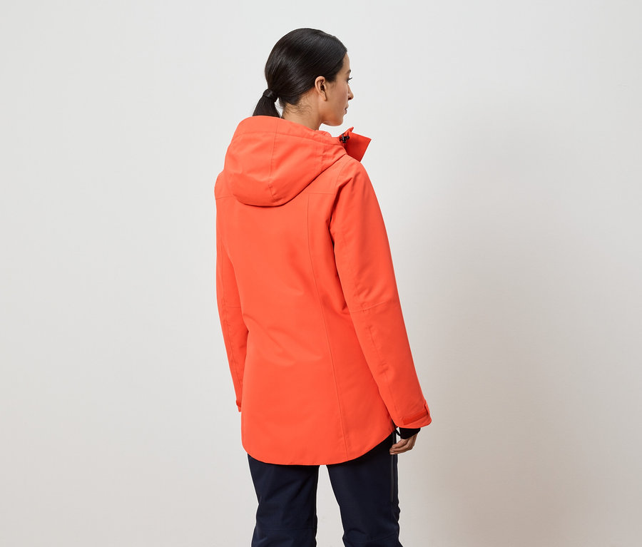 Egy nő háttal a kamerának narancssárga kapucnis kabátot visel.