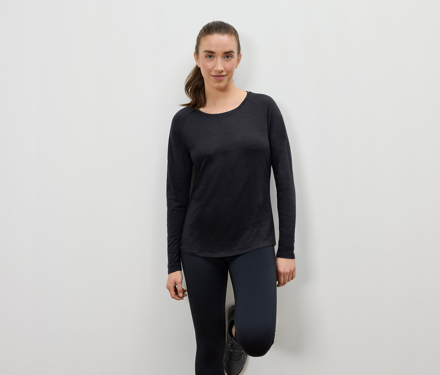 Fekete sportruházatot viselő nő a falnak támaszkodva.