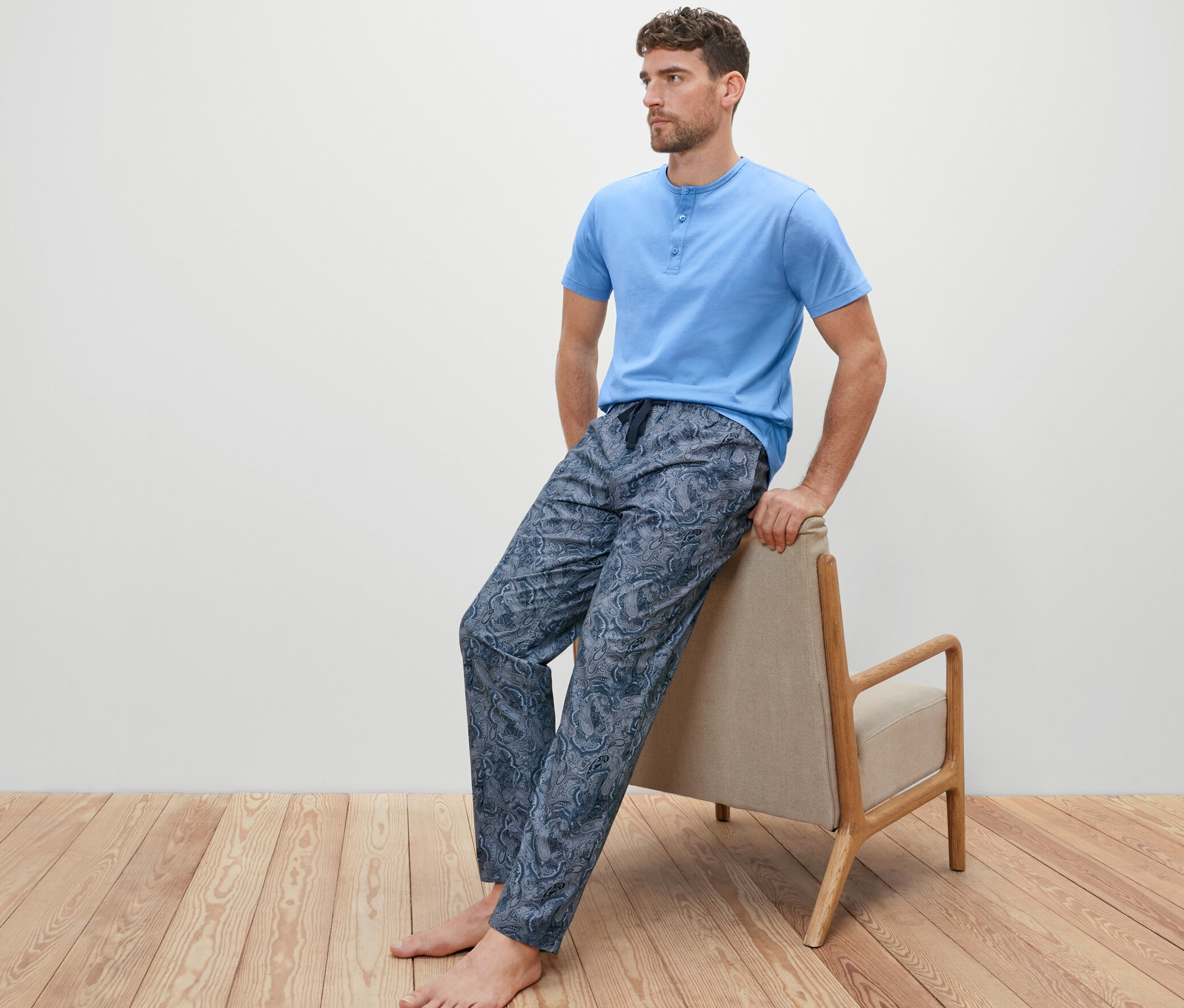 Egy férfi egy széken ül, és egy szőtt nadrágos pizsamát visel.