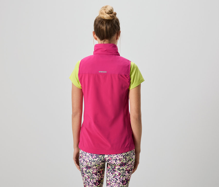 Hátulnézet egy kontyos nőről, aki rózsaszín mellényt visel egy világoszöld póló és virágmintás leggings felett.