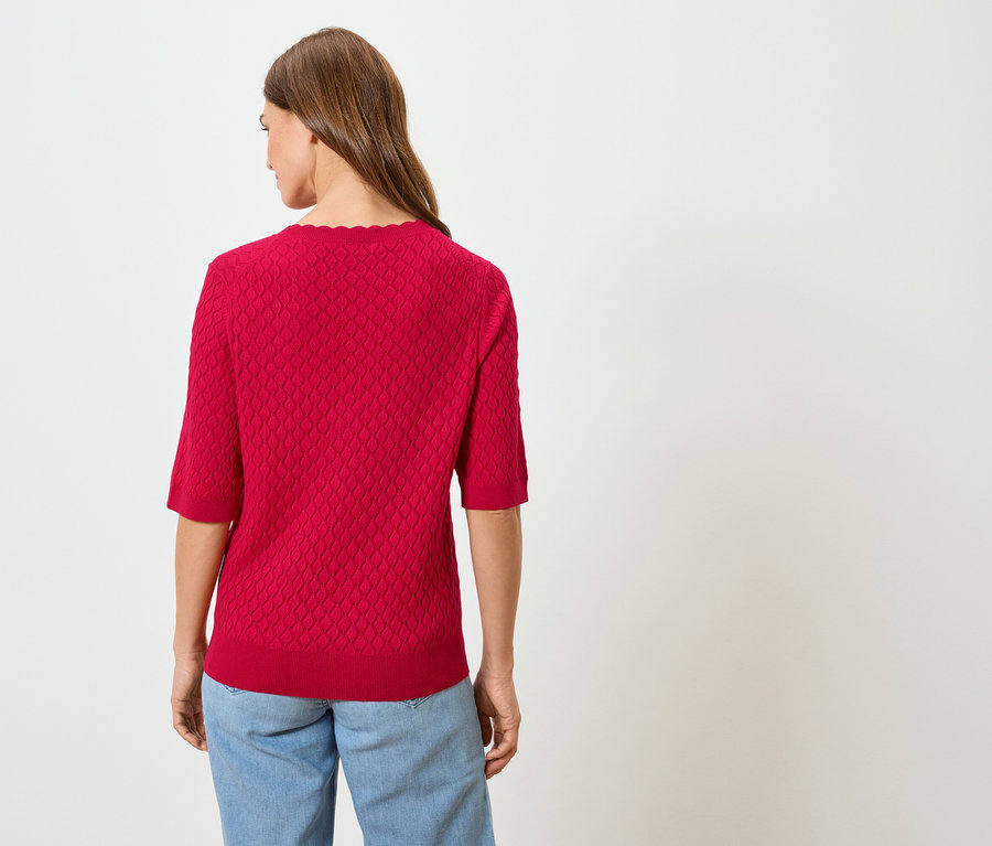 Hátulról látható egy hosszú, barna hajú nő piros pulóverben és kék farmerben.