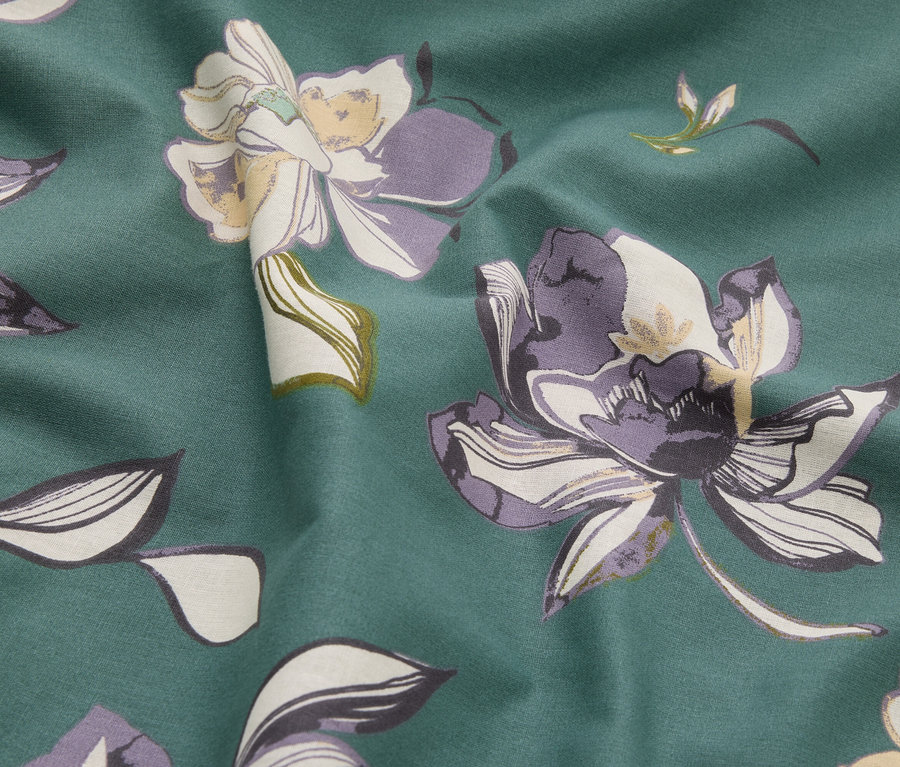 Egy zöld, lila és krémszínű virágmintás anyag közeli képe.