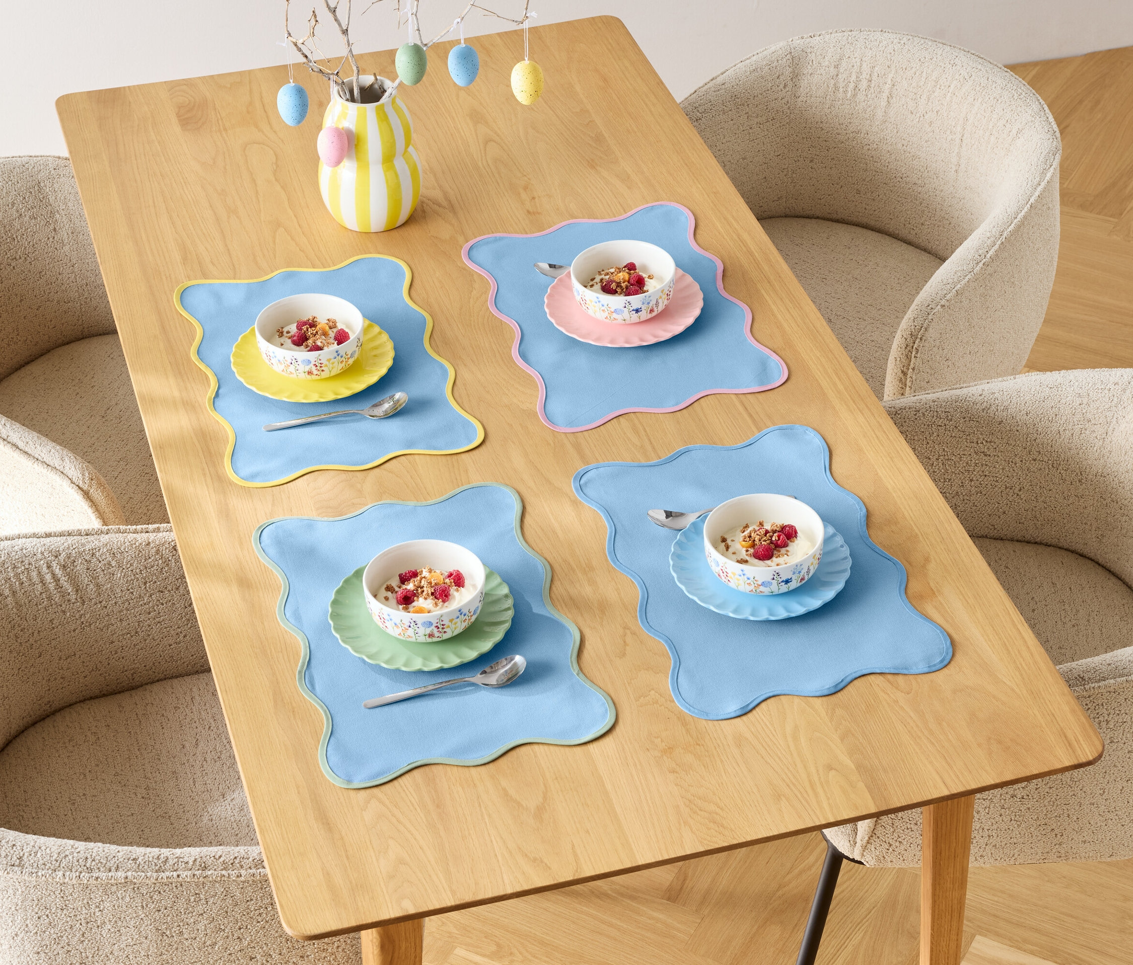 Egy étkezőasztal négy személyre van megterítve gabonapehely-tálakkal és színes alátétekkel, négy székkel körülvéve.