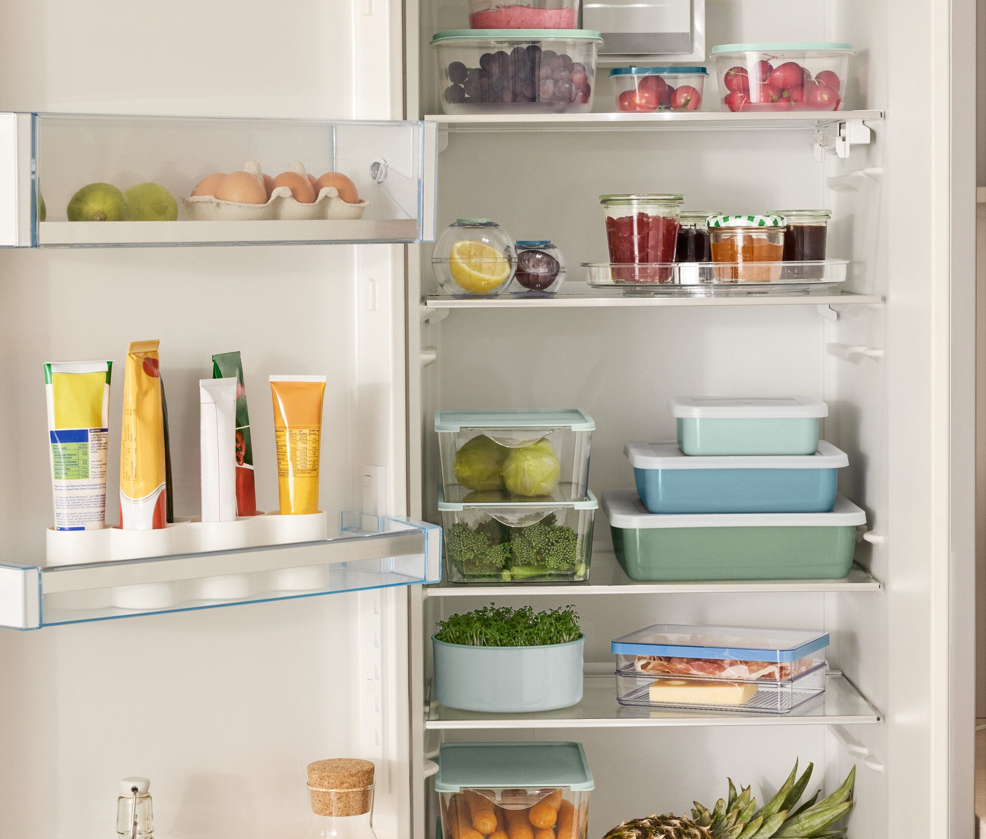 Nyitott hűtőszekrény különféle élelmiszerekkel, köztük 4 db frissentartó doboz készlettel, 2 db frissentartó gömbbel, 3 zománcozott sütőformával fedéllel és egy forgótálcával.