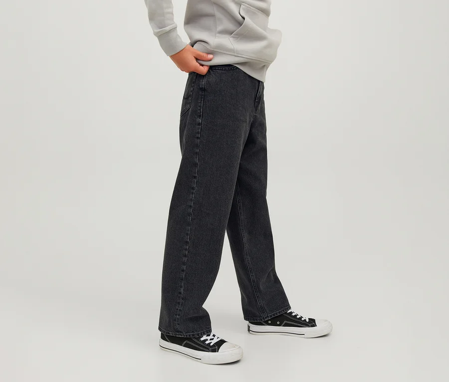 Fekete Jack&Jones JJOrginial Alex farmernadrágot, világosszürke kapucnis pulóvert és fekete-fehér sportcipőt viselő személy, egyik kezével a farmer derekát fogja.