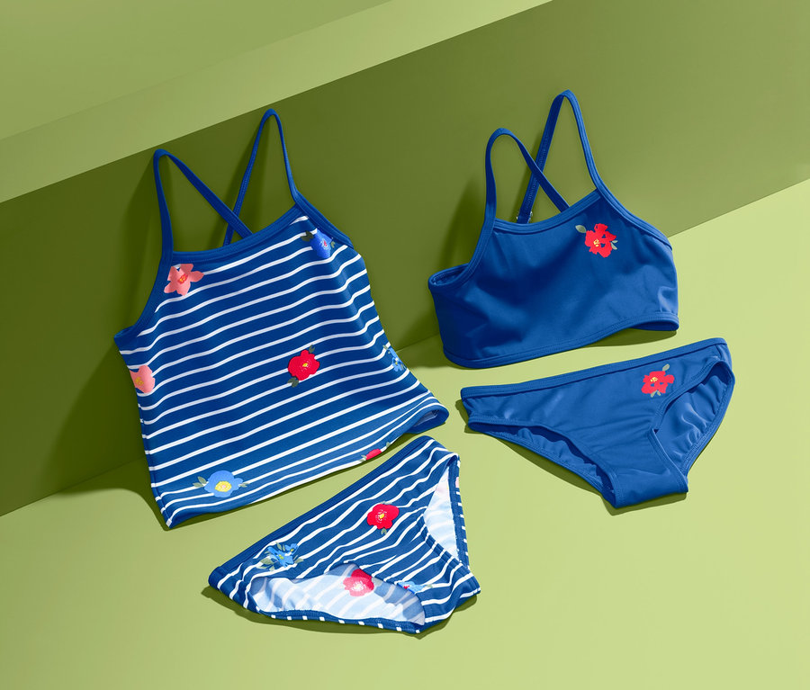 Lány tankini-bikini szett, sötétkék, piros virágokkal, zöld háttéren.