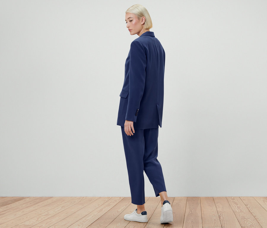 Nő pózol szövött blézerben és nadrágban.