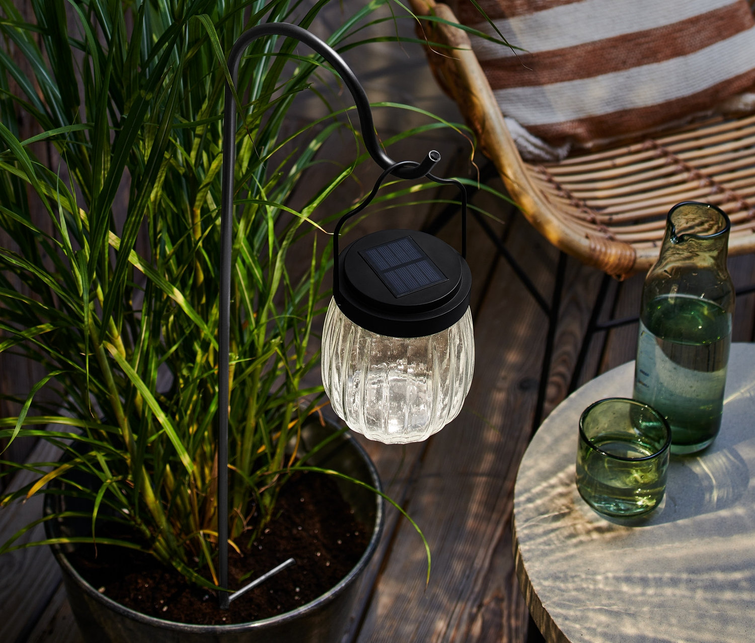 Egy napelemes leszúrható lámpa egy virágcserépben áll egy italokkal teli asztal mellett.