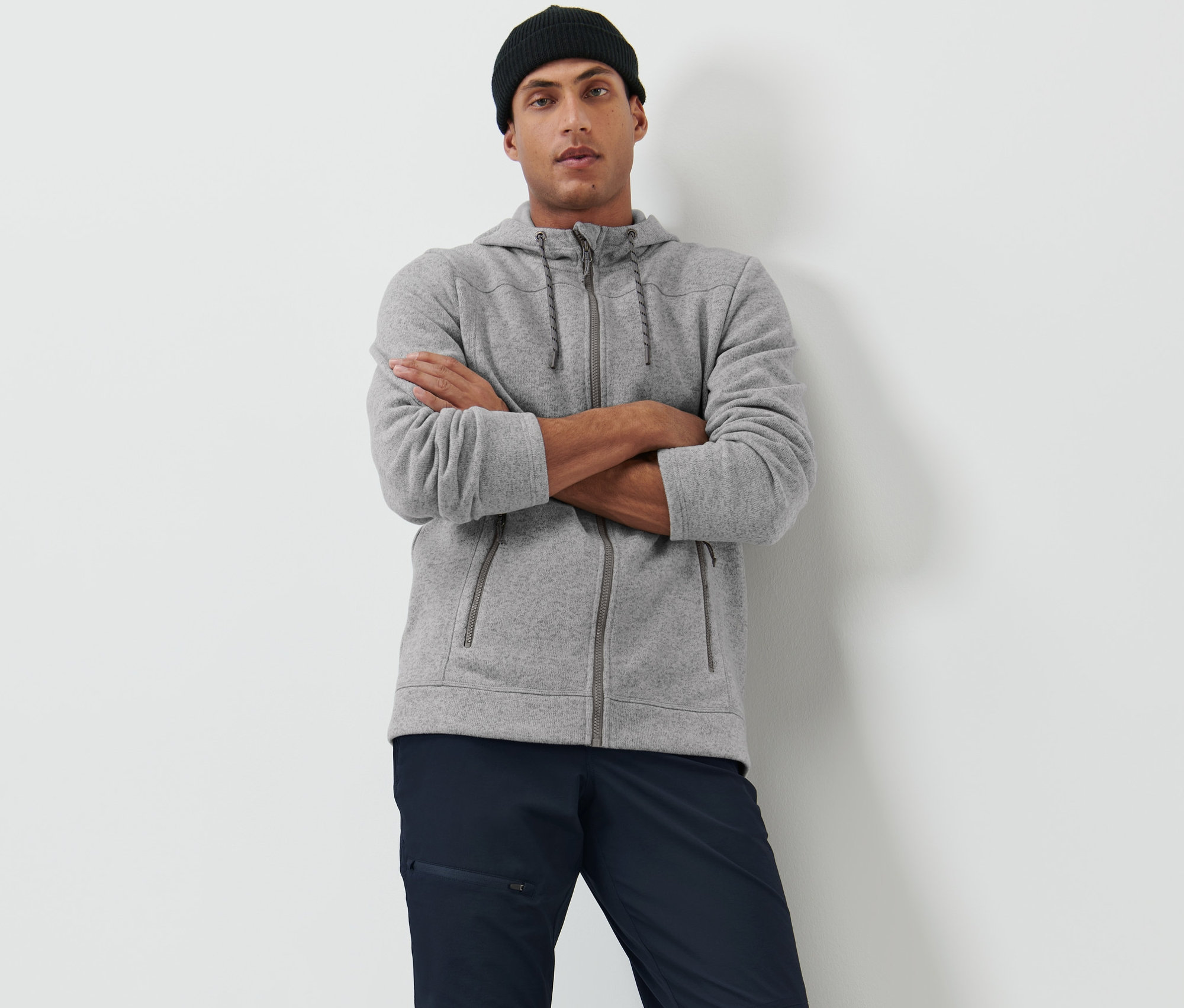 Férfi keresztbe tett karokkal pózol szürke kötött polárfelsőben és fekete sapkában.