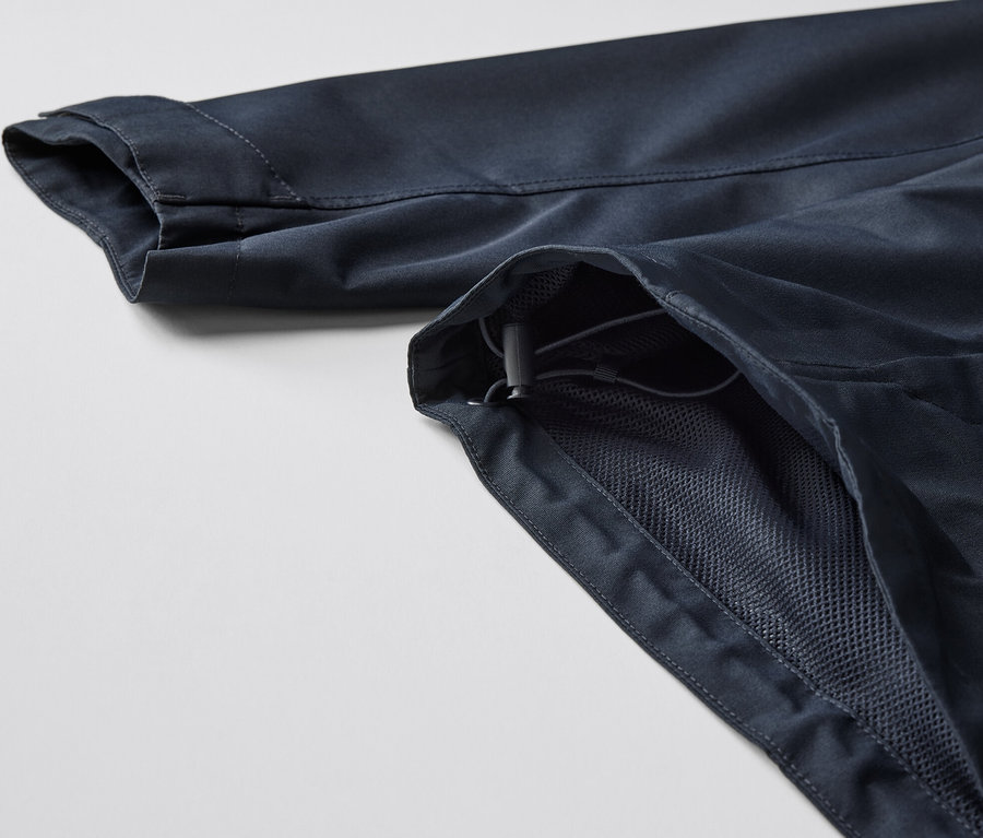 A sötétkék férfi funkcionális parka kabát részlete, a kabát ujja és a cipzár egy része látható.