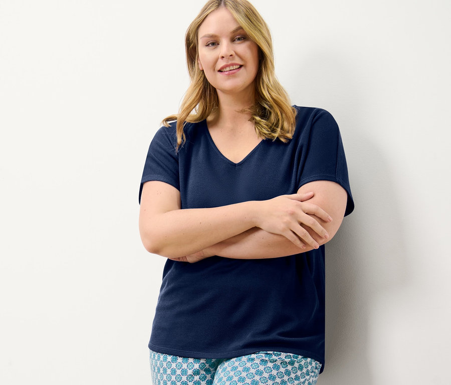 Egy nő keresztbe tett karokkal pózol egy sötétkék strukturált felsőben és egy mintás női jerseynadrágban.