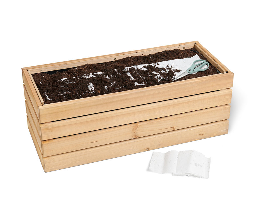 Földdel, vetőmagszőnyeggel és ollóval teli fa virágláda. A virágládában egy Méhlegelő vetőmagszőnyeg látható.