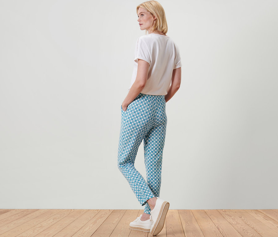 Egy szőke nő háttal áll a kamerának, és mintás női jerseynadrágot visel.