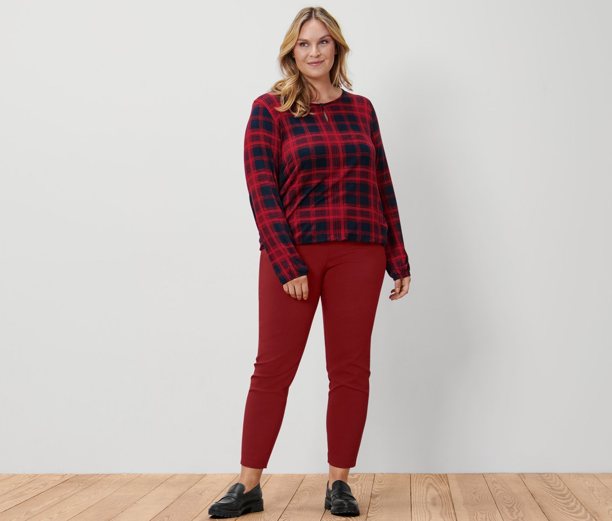 Egy nő kockás női pólóblúzt, piros sztreccsnadrágot és fekete bőr mokaszint visel.